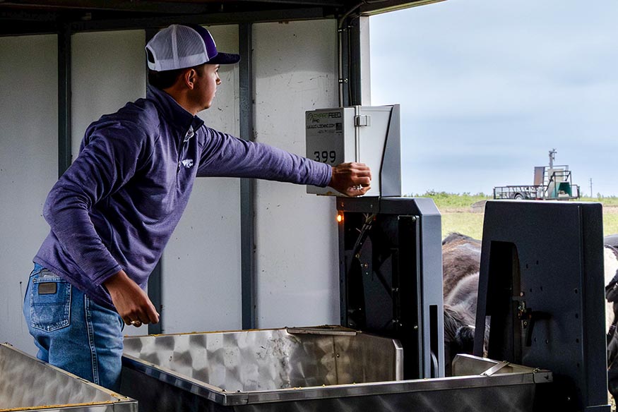Graduate research assistant Jace Owen inspecting the SmartFeed Pro system trailer used in cattle supplementation research at Rannells Ranch